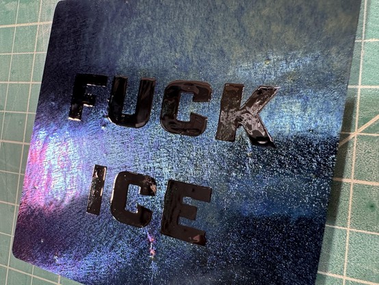 Dichroic black glass square with “fuck ice” stenciled in an over glaze.